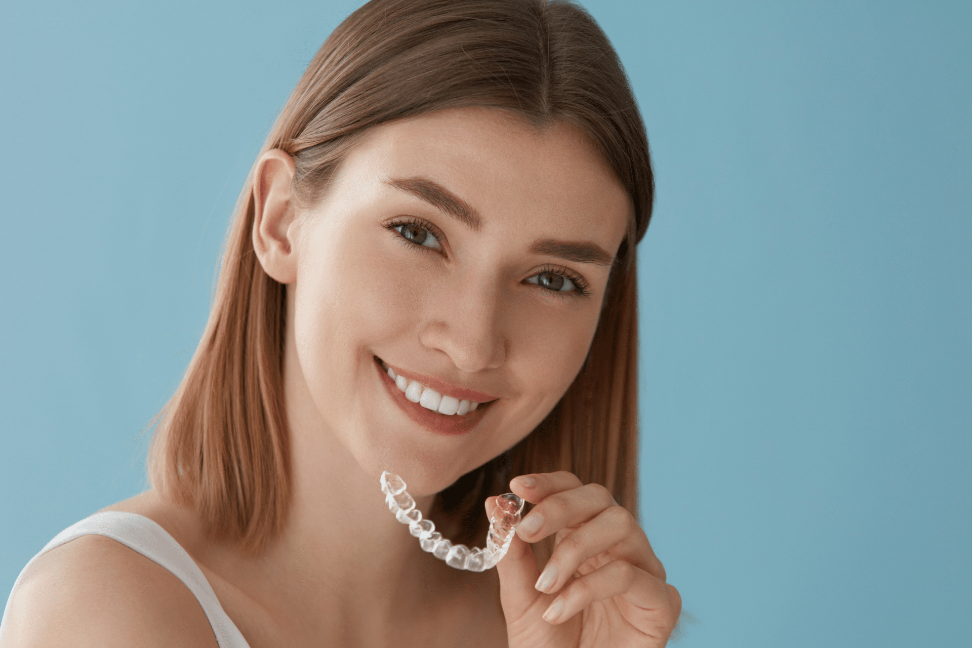 Smiling woman holding a clear aligner against a blue background