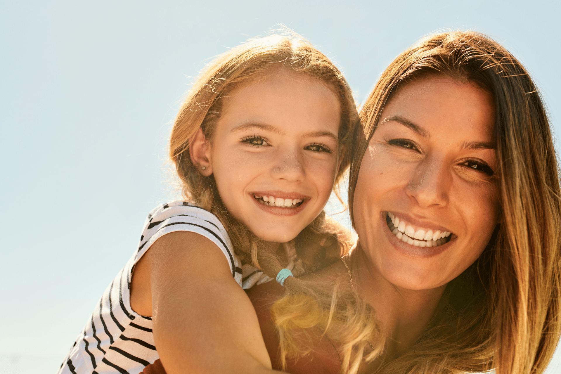 Mother and young daughter with bright, healthy smiles hugging outdoors.